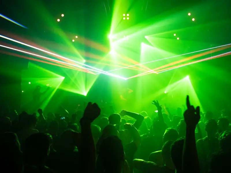 People dancing under green club lights (symbol image)